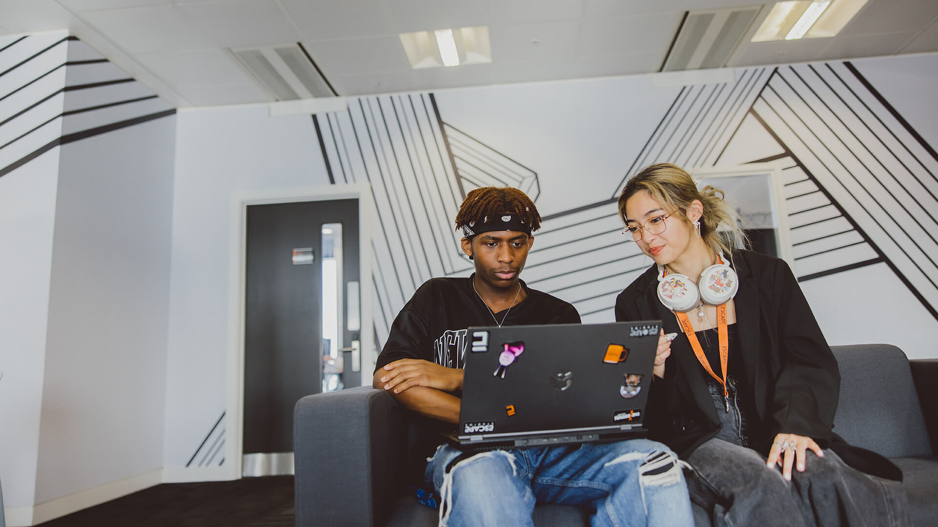 Two students sat on a sofa in the breakout space with a laptop